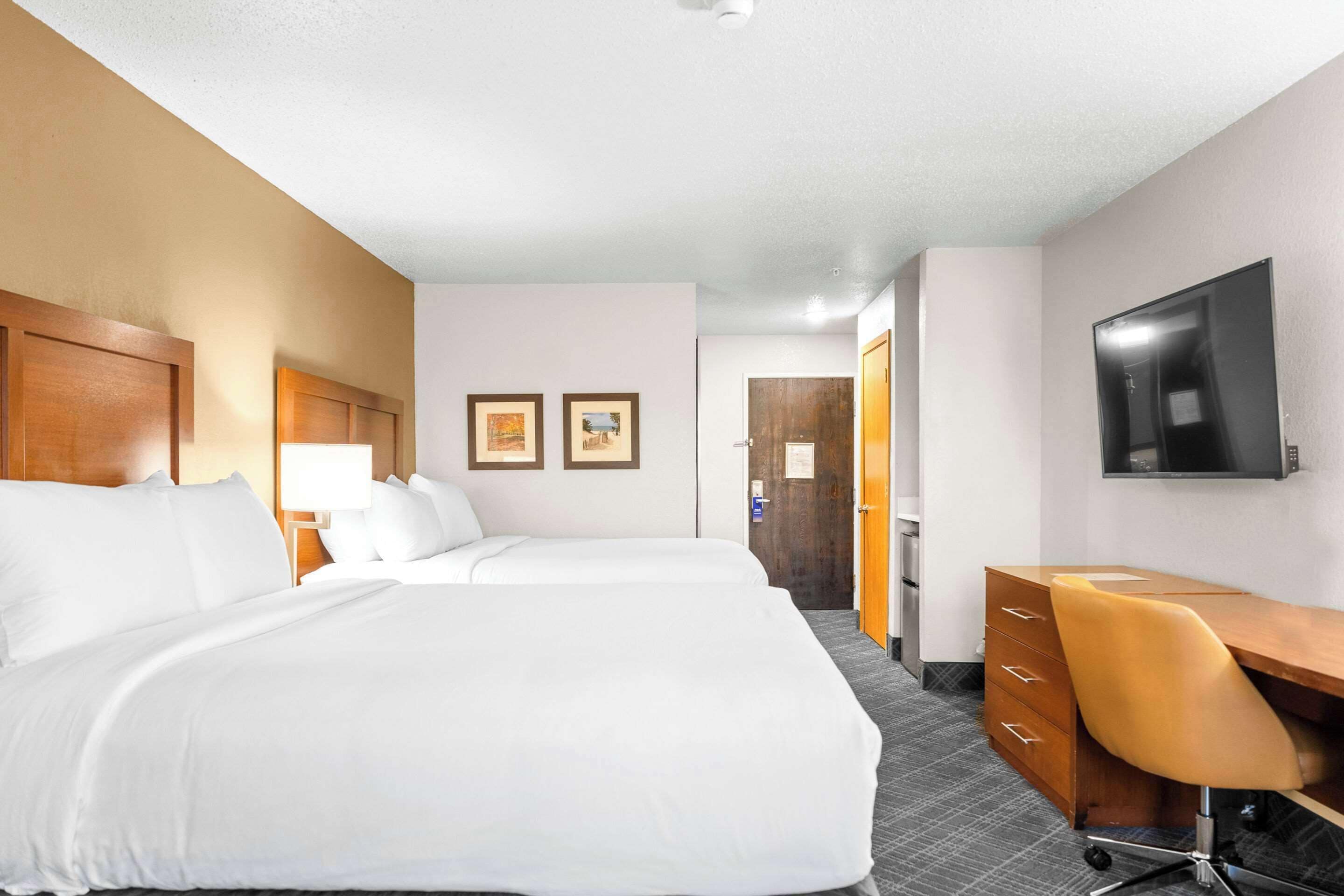 A hotel room with two beds, a desk, a chair, a TV, and a door leading to a bathroom.