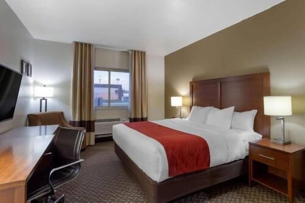 A hotel room with a bed, a desk, a chair, a TV, and a window with curtains.