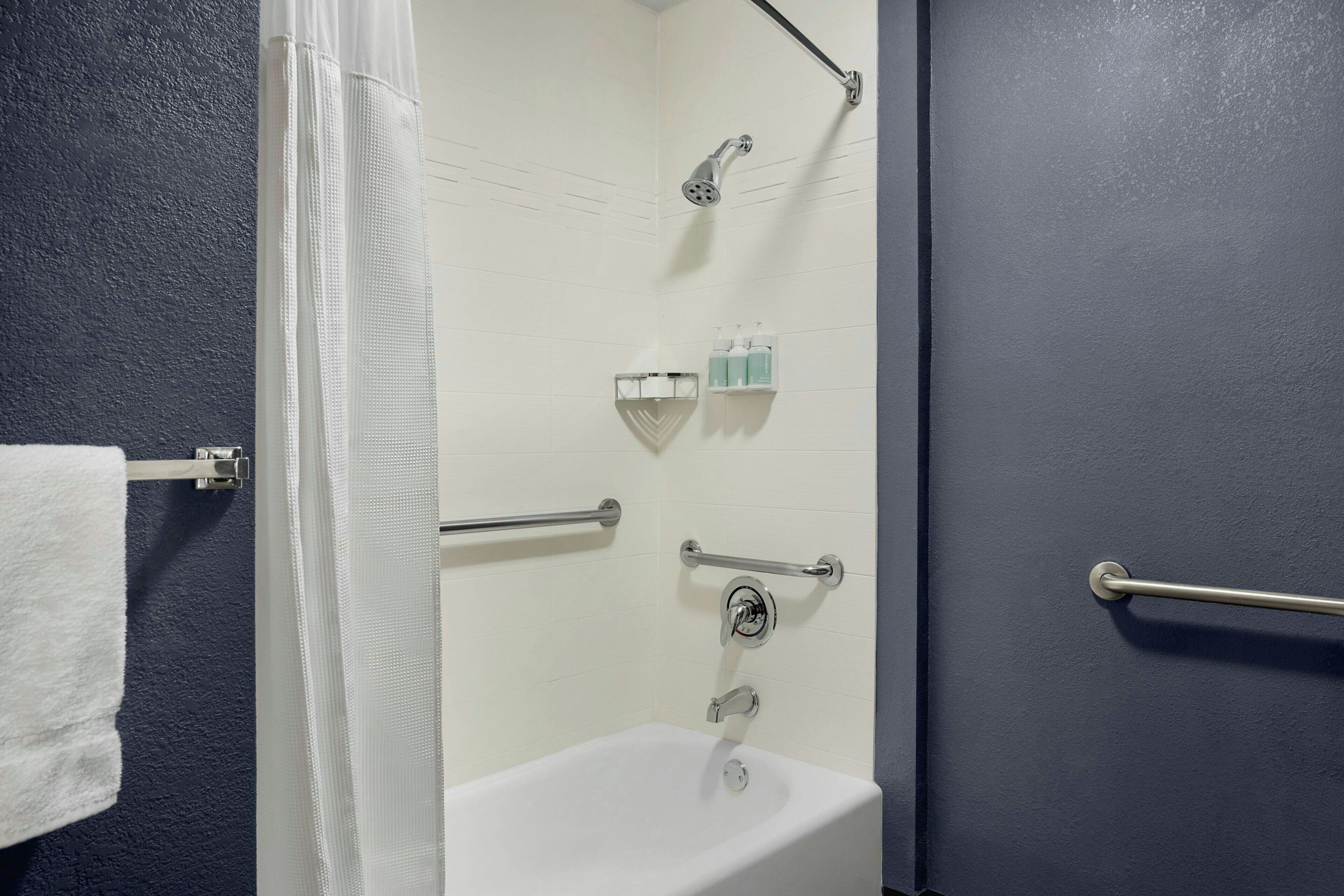 A bathroom with a bathtub, shower, and handrails.