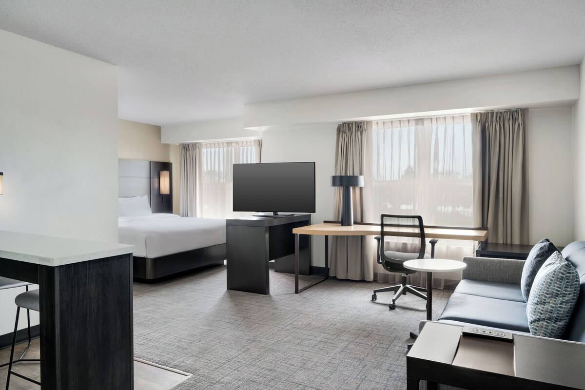 Een moderne hotelkamer met een bed, bureau, televisie, bank en een klein tafeltje.