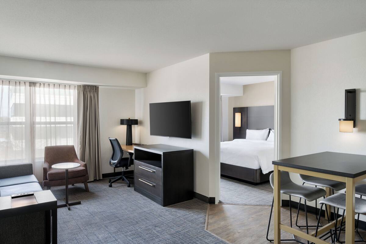 Een hotelkamer met een bed, bureau, stoel, televisie en uitzicht op het exterieur.