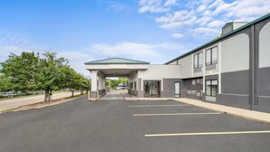 A parking lot leading to a building with a covered entrance, a clear sky, and trees on the left. - Quality Inn Auburn Campus Area I-85 (Auburn)