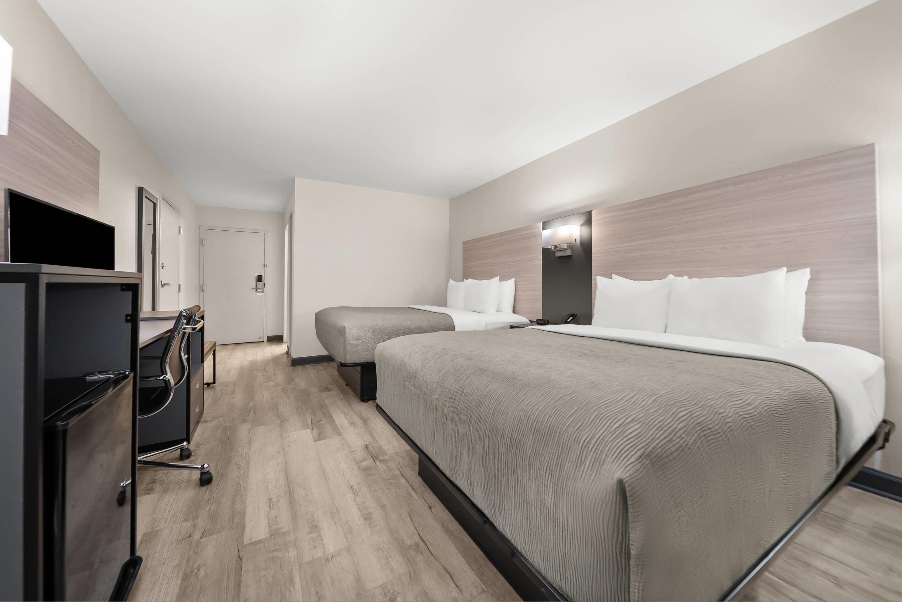 A hotel room with a bed, a desk with a chair, a TV, and a wardrobe.