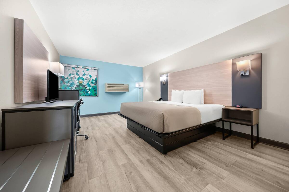 A modern hotel room with a bed, desk, and a wall-mounted TV.