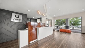 A hotel reception area with a modern design, featuring a reception desk, a sign indicating 'Quality by Choice Hotels', and a large window offering a view of the outdoors. - Quality Inn Auburn Campus Area I-85 (Auburn)