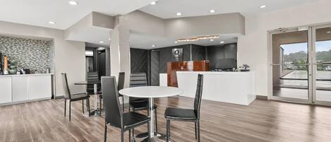 Une cuisine moderne dotée d’un îlot central, d’un coin repas avec une table ronde et des chaises, et d’une grande fenêtre offrant une vue sur l’extérieur.