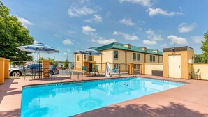 A swimming pool with lounge chairs and umbrellas, surrounded by a building with a green roof and beige walls. - Quality Inn Auburn Campus Area I-85 (Auburn)