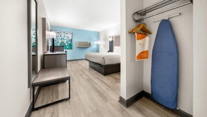 A hotel room with a bed, a desk, a mirror, a hanging clothes rack, and a blue surfboard. - Quality Inn Auburn Campus Area I-85 (Auburn)