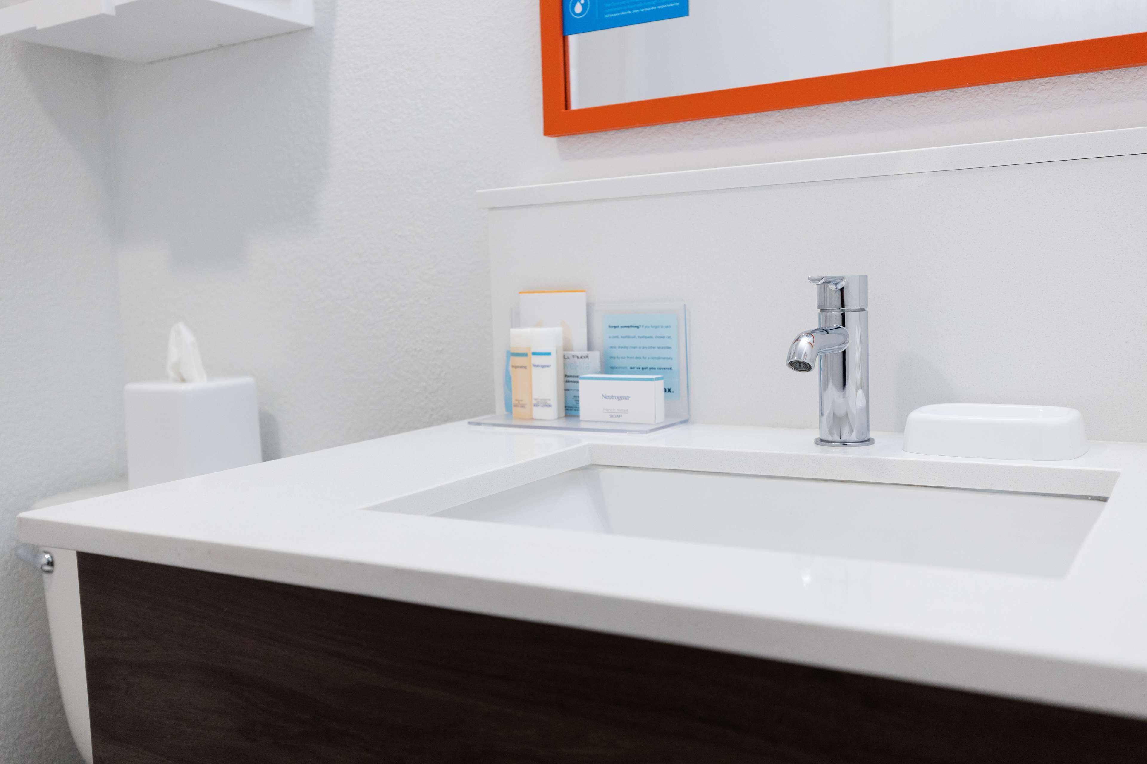 A bathroom with a white sink, a mirror with an orange frame, and toiletries on the counter.