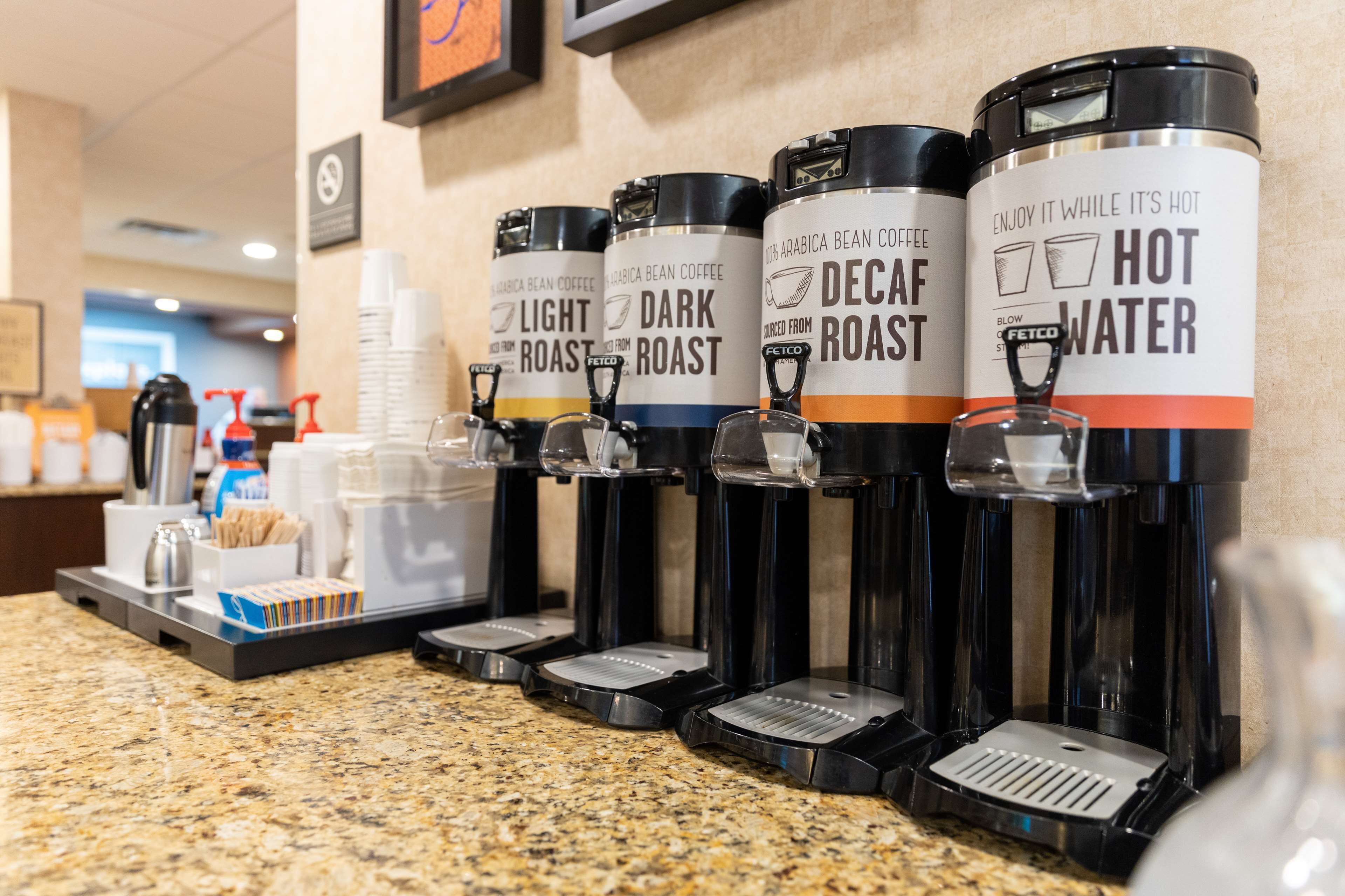 Estación de café con dispensadores etiquetados como 'Tueste Suave', 'Tueste Oscuro', 'Tueste Descafeinado' y 'Agua Caliente'.