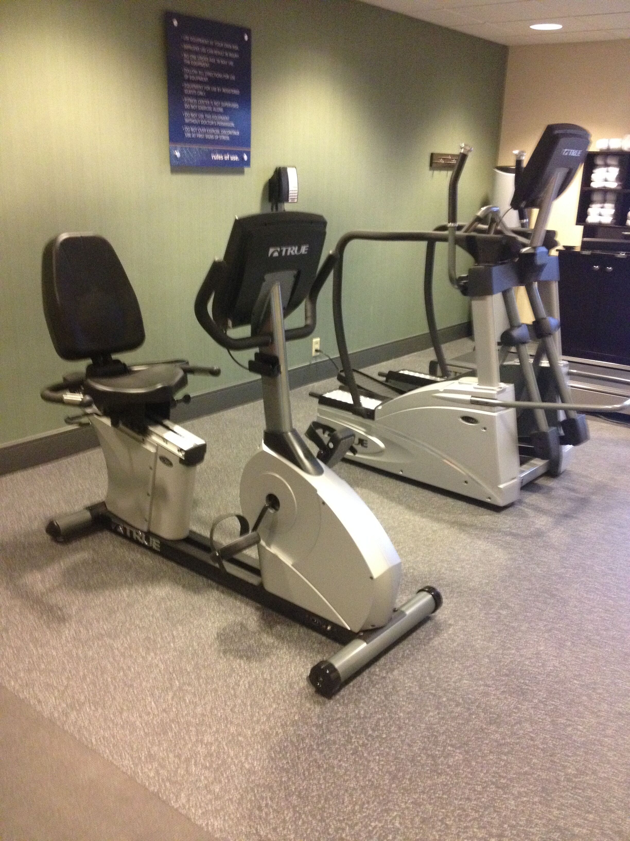 A fitness area with cardio machines, including an elliptical and a stationary bike, and a wall-mounted exercise bike.