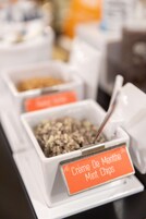 Un bar de aperitivos con recipientes etiquetados, que incluyen un cartel que dice 'Crème De Menthe Mint Chips'.