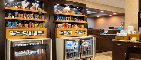 A hotel snack bar with shelves stocked with snacks and a refrigerated display case.