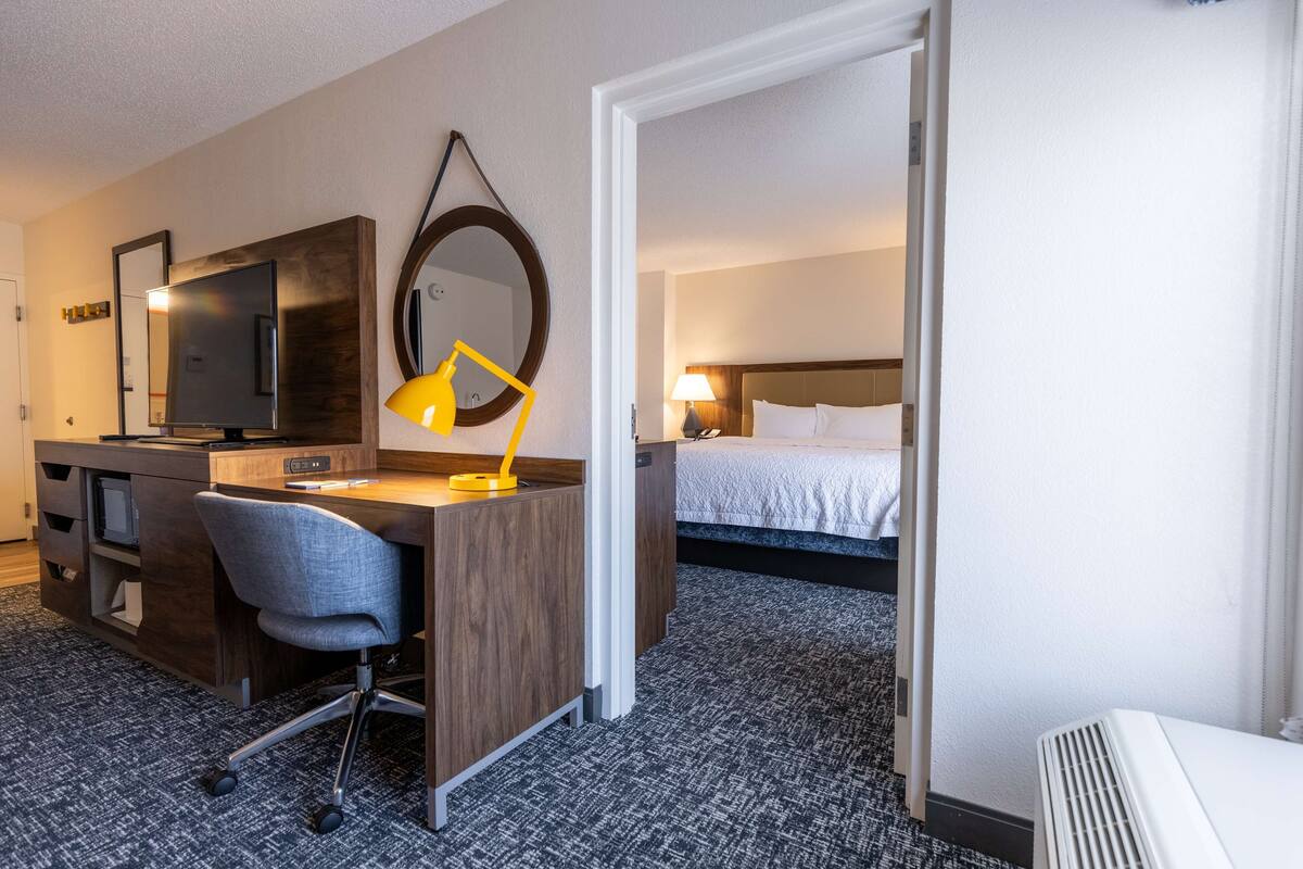 A hotel room with a desk, chair, bed, and a mirror.
