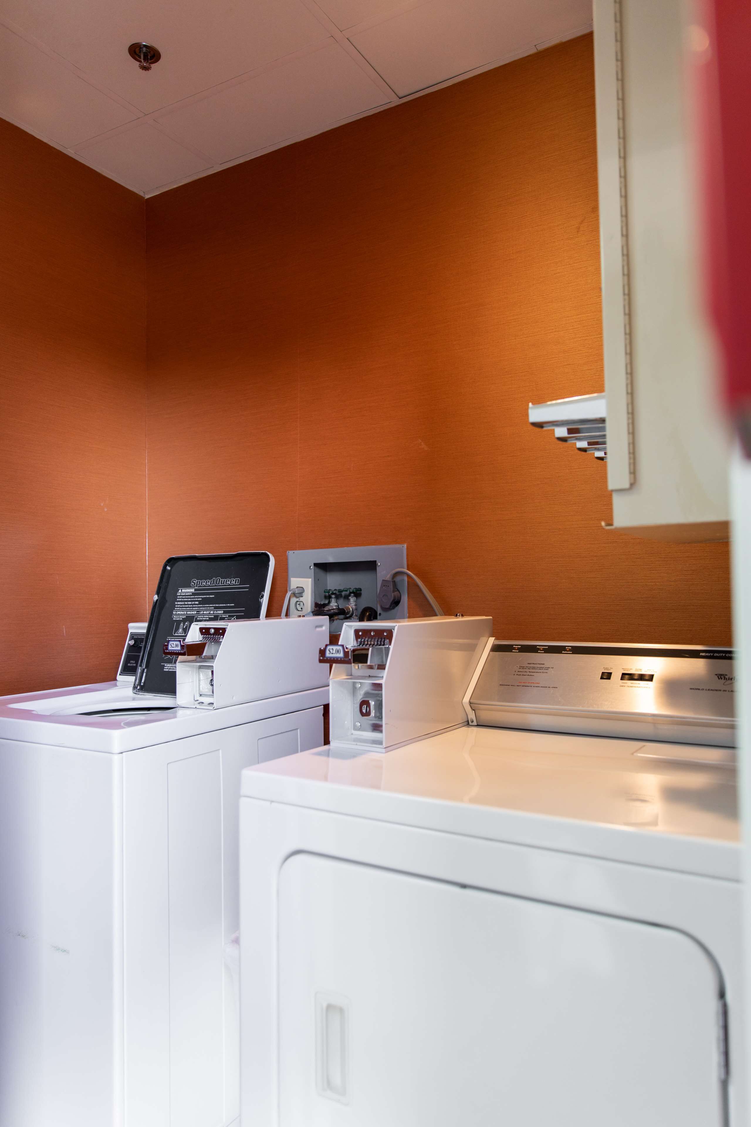A laundry room with two washing machines and a dryer, a control panel, and a wall-mounted cabinet.