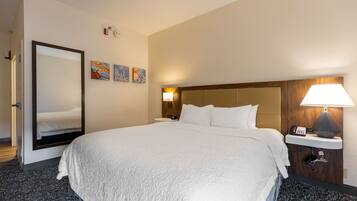 A hotel room with a large bed, a mirror, a nightstand with a lamp, and three artwork pieces on the wall.