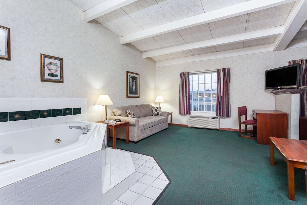 A hotel room with a large bathtub, a sofa, a television, and a desk.