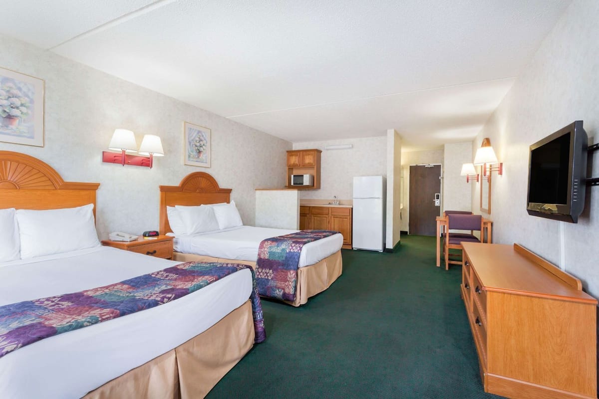 A hotel room with two beds, a kitchenette, a television, and a desk.