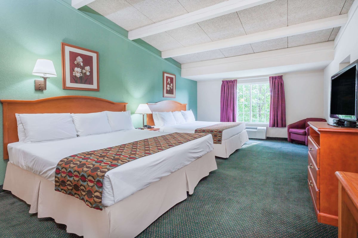 A hotel room with two beds, a television, a desk, and a window with curtains.