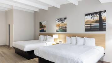 Habitación de hotel con dos camas, cabecero de madera, mesita de noche con lámpara y tres cuadros de paisajes en la pared.