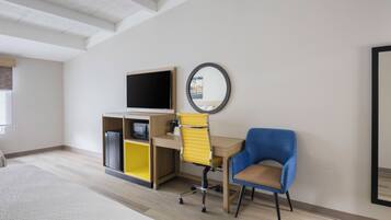 A hotel room with a bed, a desk with a chair, a television, and a mirror on the wall.
