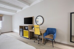 Una habitación de hotel con una cama, un escritorio con una silla, un televisor y un espejo en la pared.