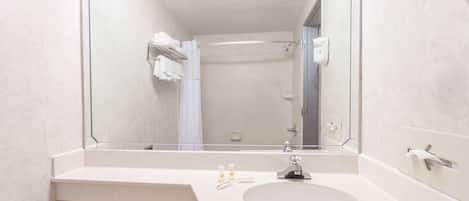 A bathroom with a large mirror, a sink, and a shower area.