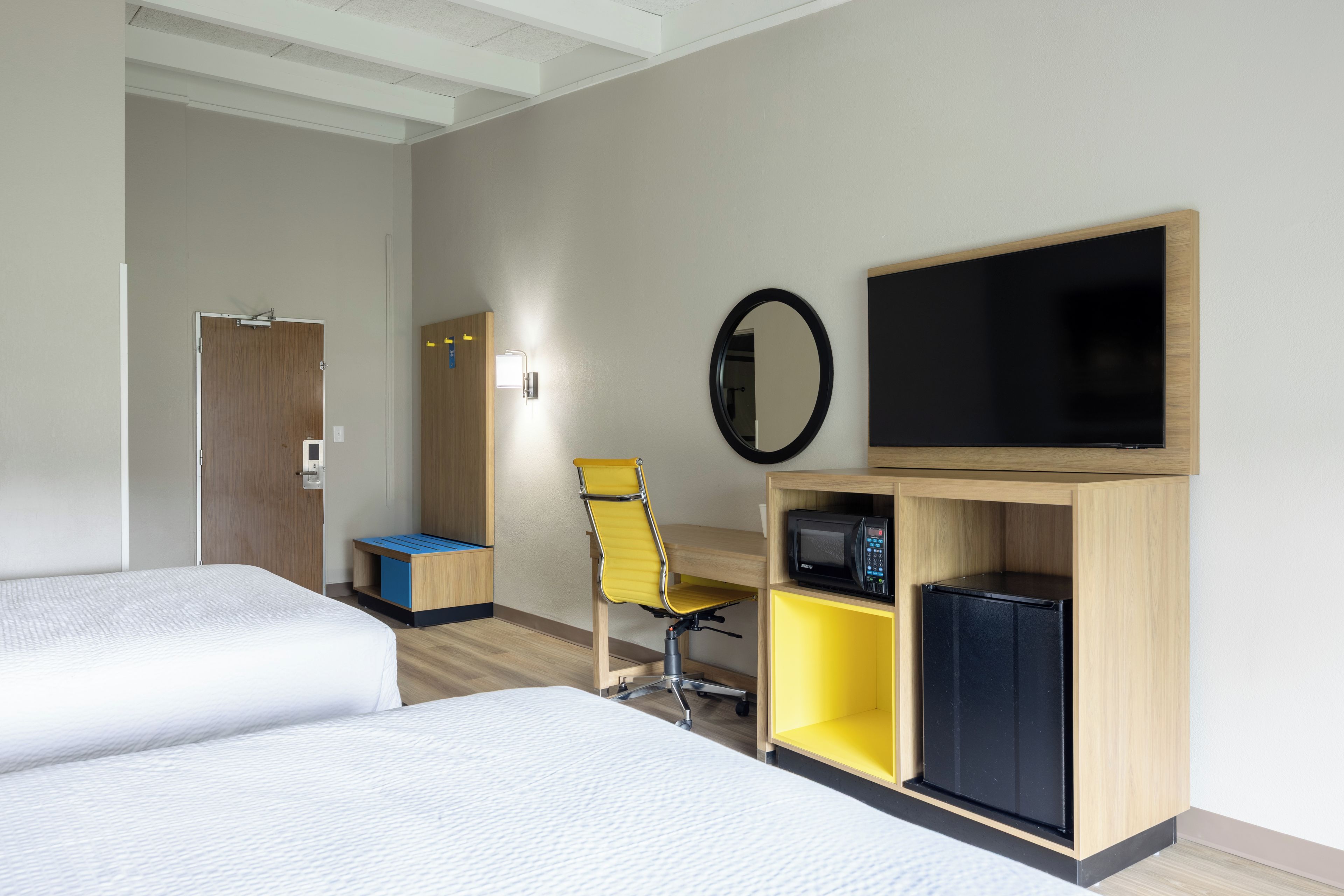 A hotel room with two beds, a desk, a chair, a television, and a microwave.