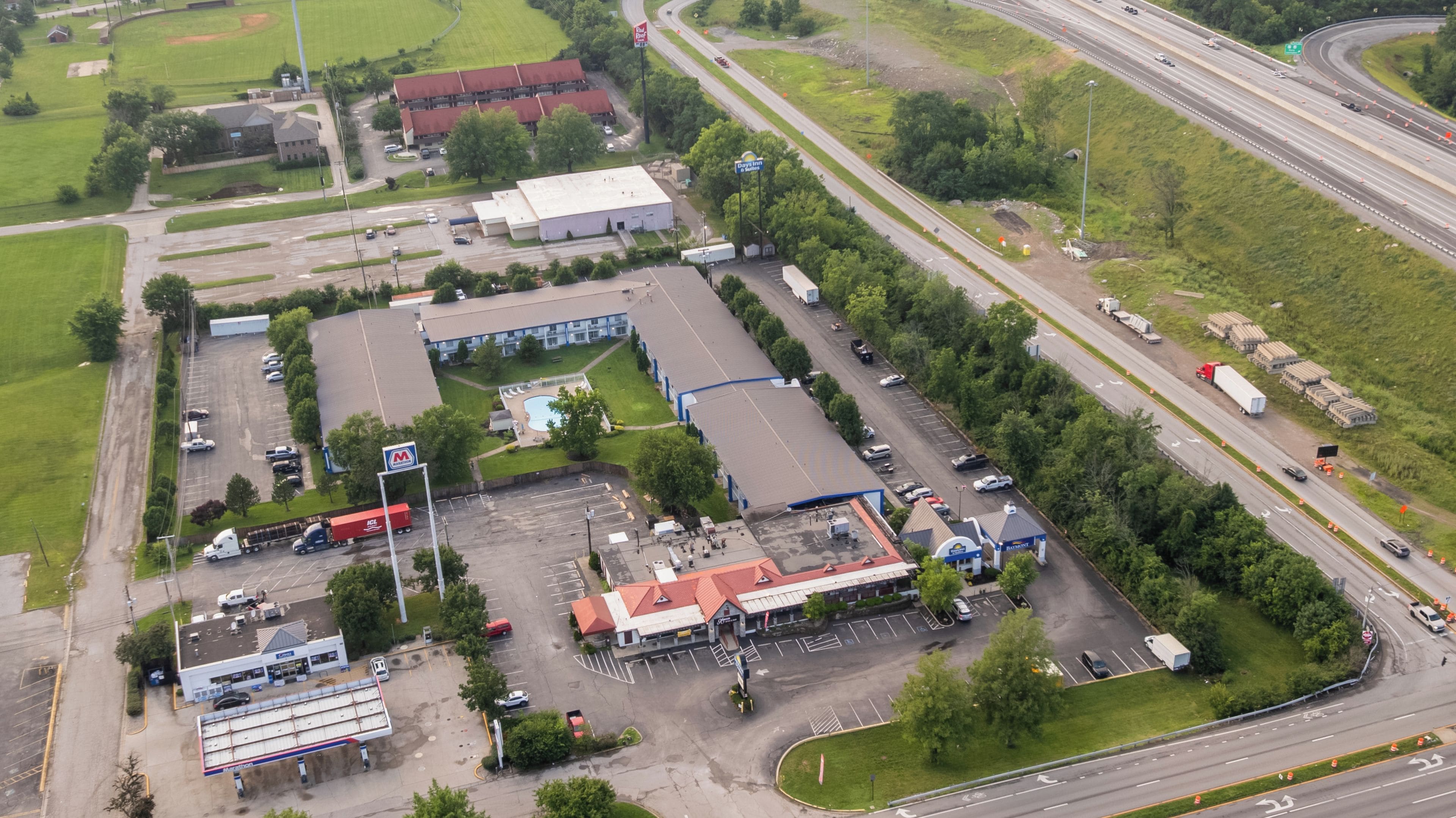 Vue aérienne d’une zone commerciale comprenant un parking, une station-service et un grand bâtiment doté d’un toit rouge.