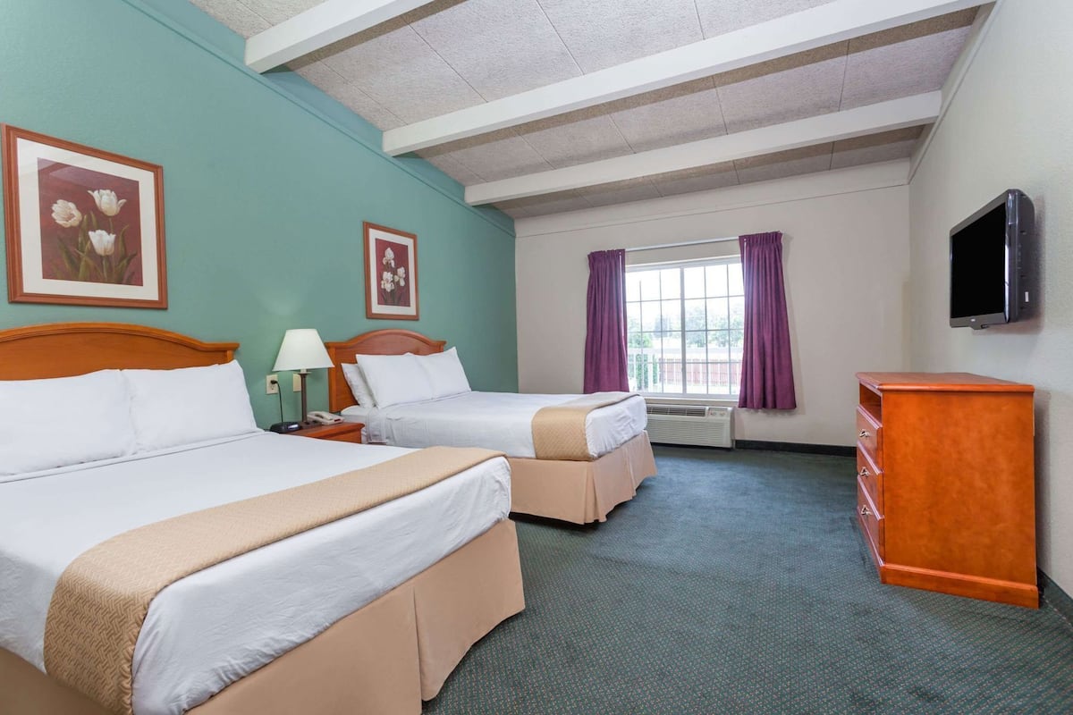 A hotel room with two beds, a desk, a TV, and a window with curtains.