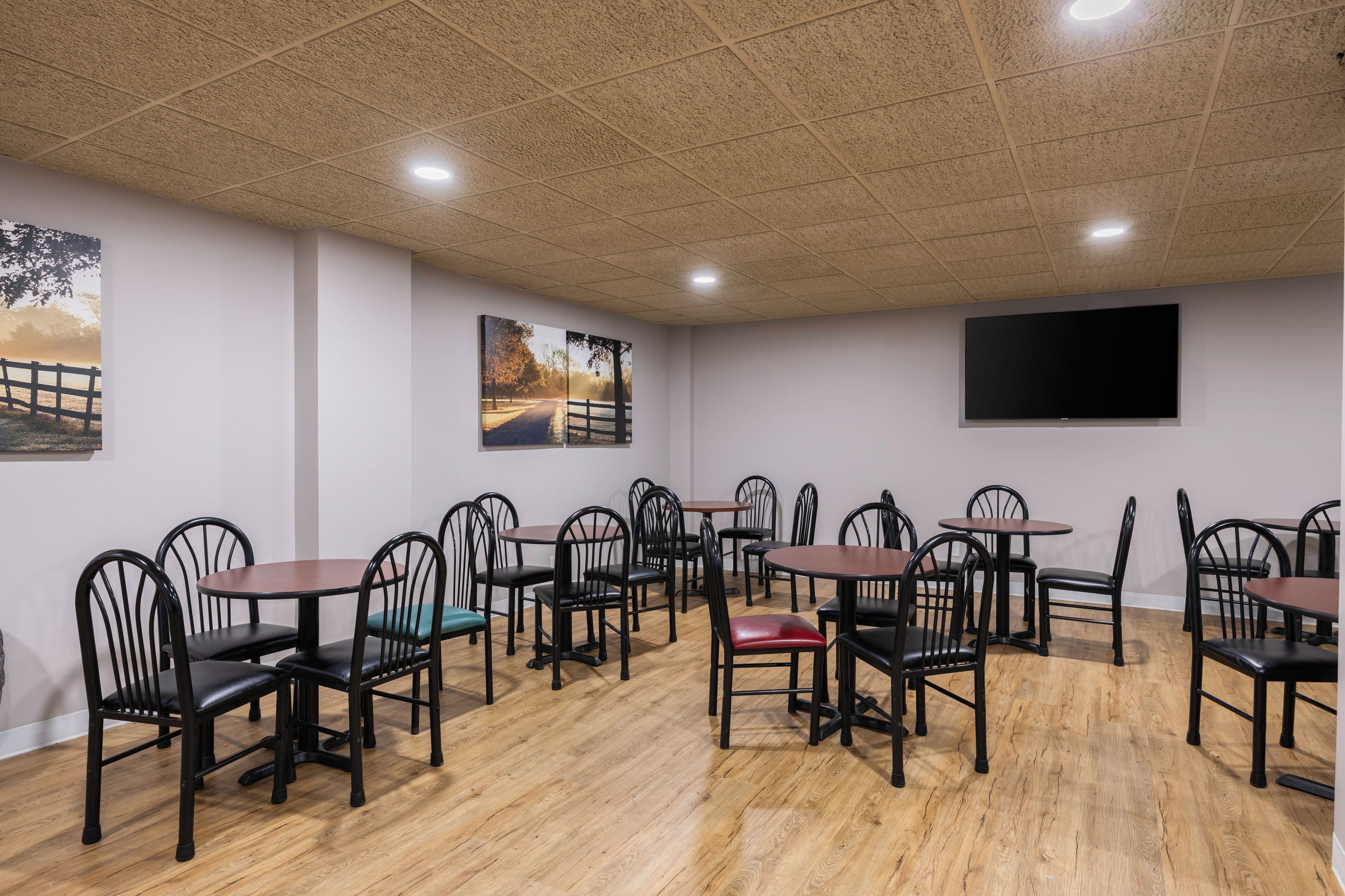 Un comedor con varias mesas y sillas, piso de madera e iluminación empotrada en el techo.