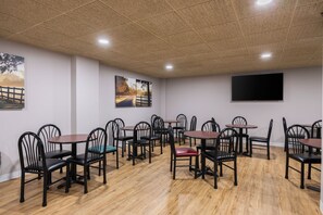 Uma sala de jantar com várias mesas e cadeiras, piso de madeira e teto com iluminação embutida.