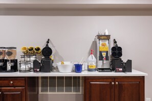 Una encimera de cocina con máquinas para hacer gofres, dispensadores de masa para gofres y una plancha para gofres.
