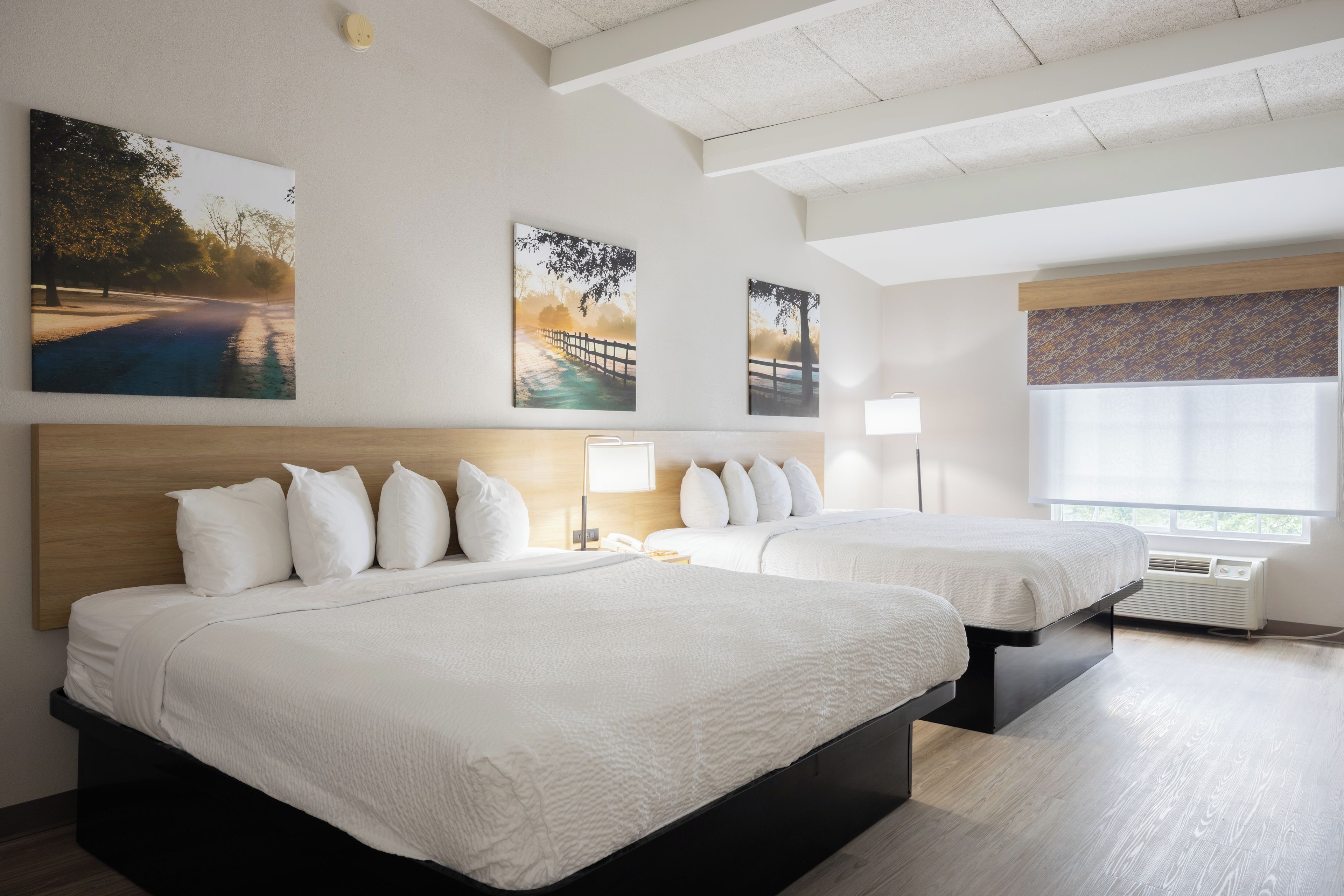 Habitación de hotel con dos camas, un ventanal grande y tres cuadros colgados en la pared.