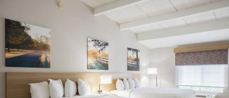 Habitación de hotel con dos camas, un ventanal grande y tres cuadros colgados en la pared.
