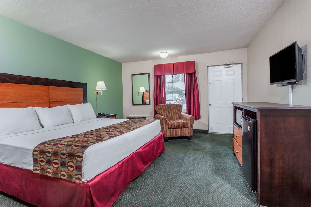 A hotel room with a bed, a chair, a desk, a television, and a door.