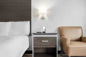 Una habitación de hotel con una cama, una mesita de noche con lámpara y un sillón de cuero.