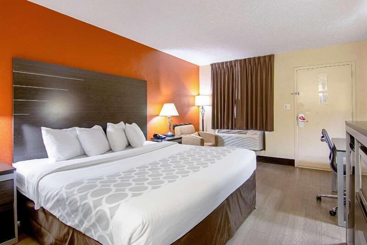 A hotel room with a large bed, a desk, a chair, a lamp, and a door.