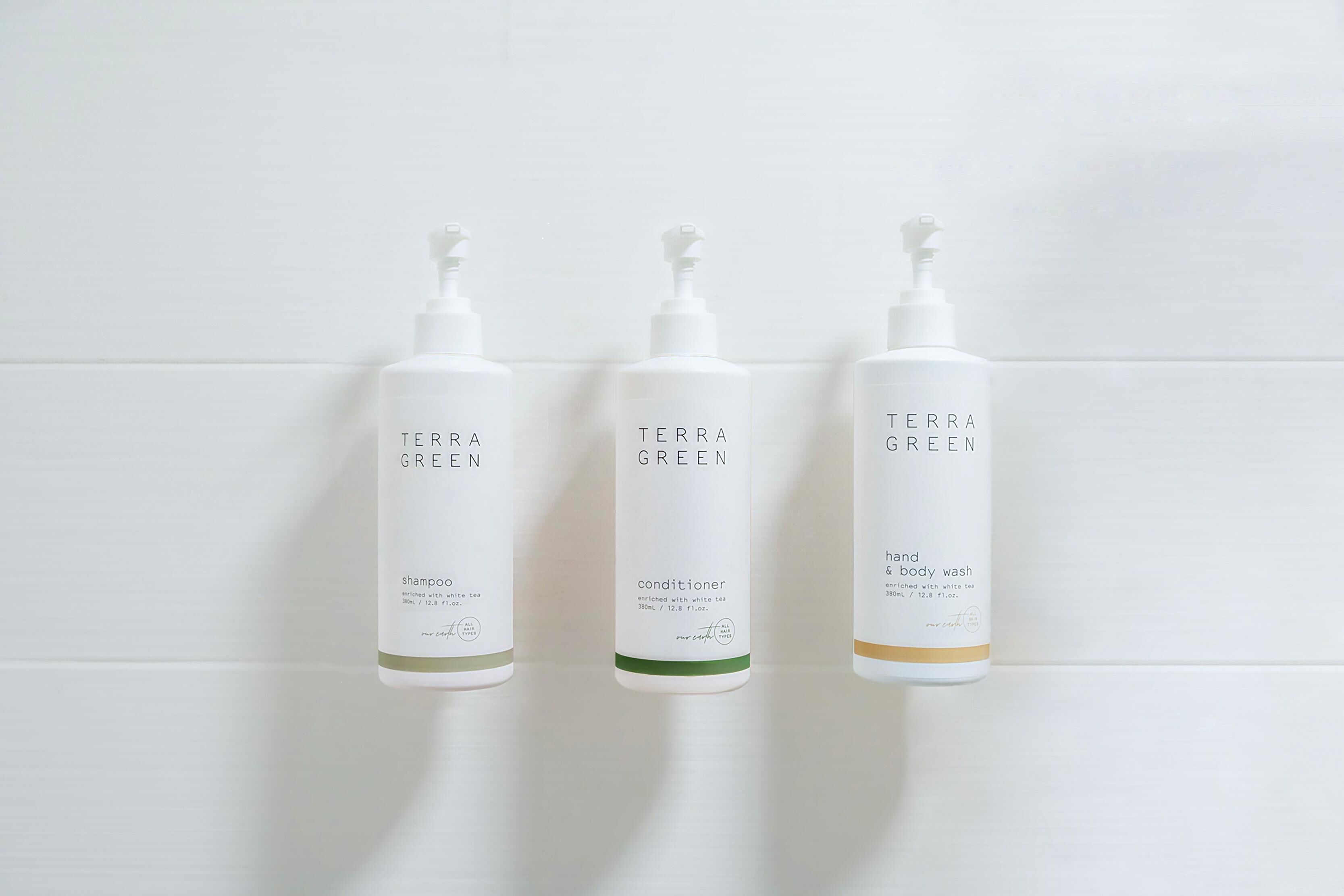 Tres botellas de productos Terra Green sobre una pared de baldosas blancas.