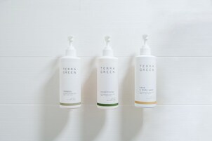 Tres botellas de productos Terra Green sobre una pared de baldosas blancas.