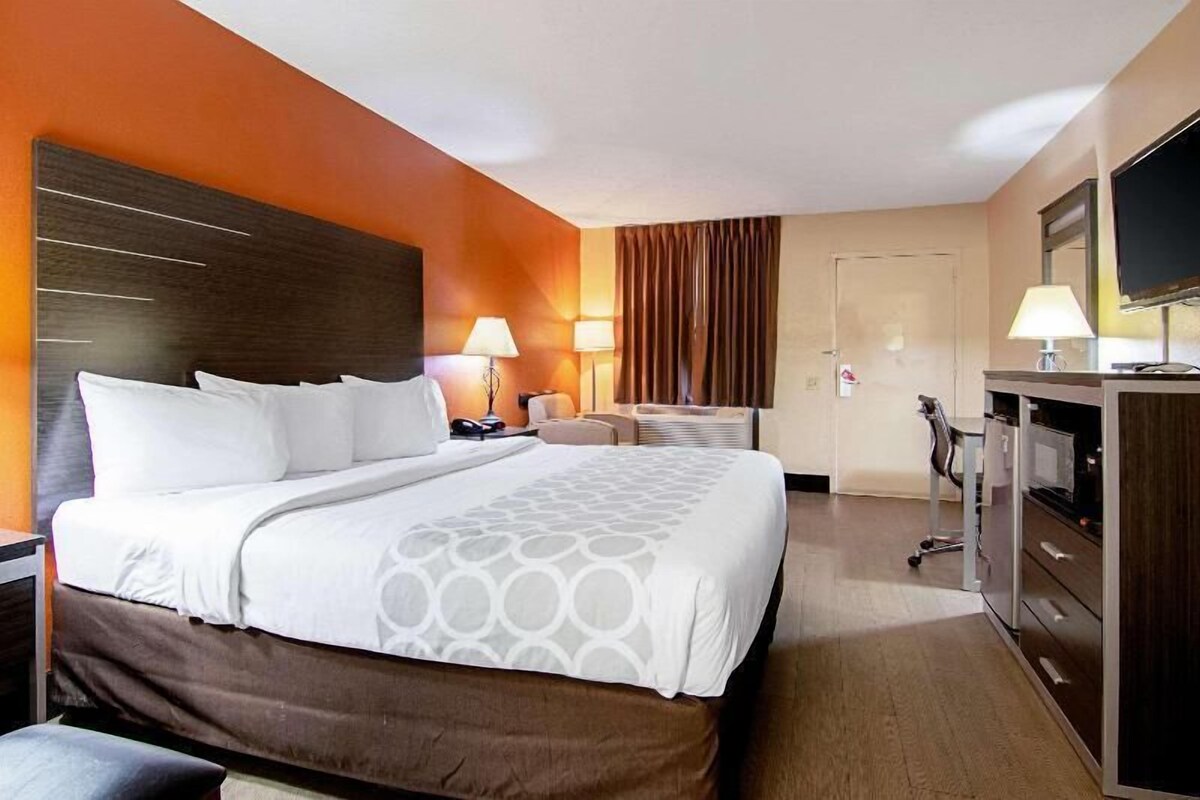 A hotel room with a large bed, a desk with a chair, a television, and a desk lamp.