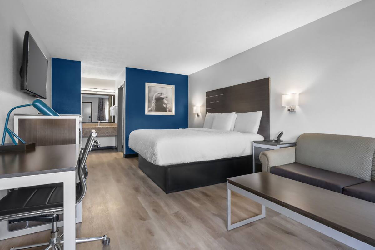 Ein modernes Hotelzimmer mit Bett, Schreibtisch, Sessel, Sofa und Fernseher.