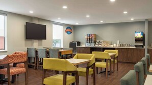 A restaurant with wooden tables and chairs, a counter with a coffee machine, and a television mounted on the wall. - Baymont by Wyndham Georgetown/Lexington North (Georgetown)