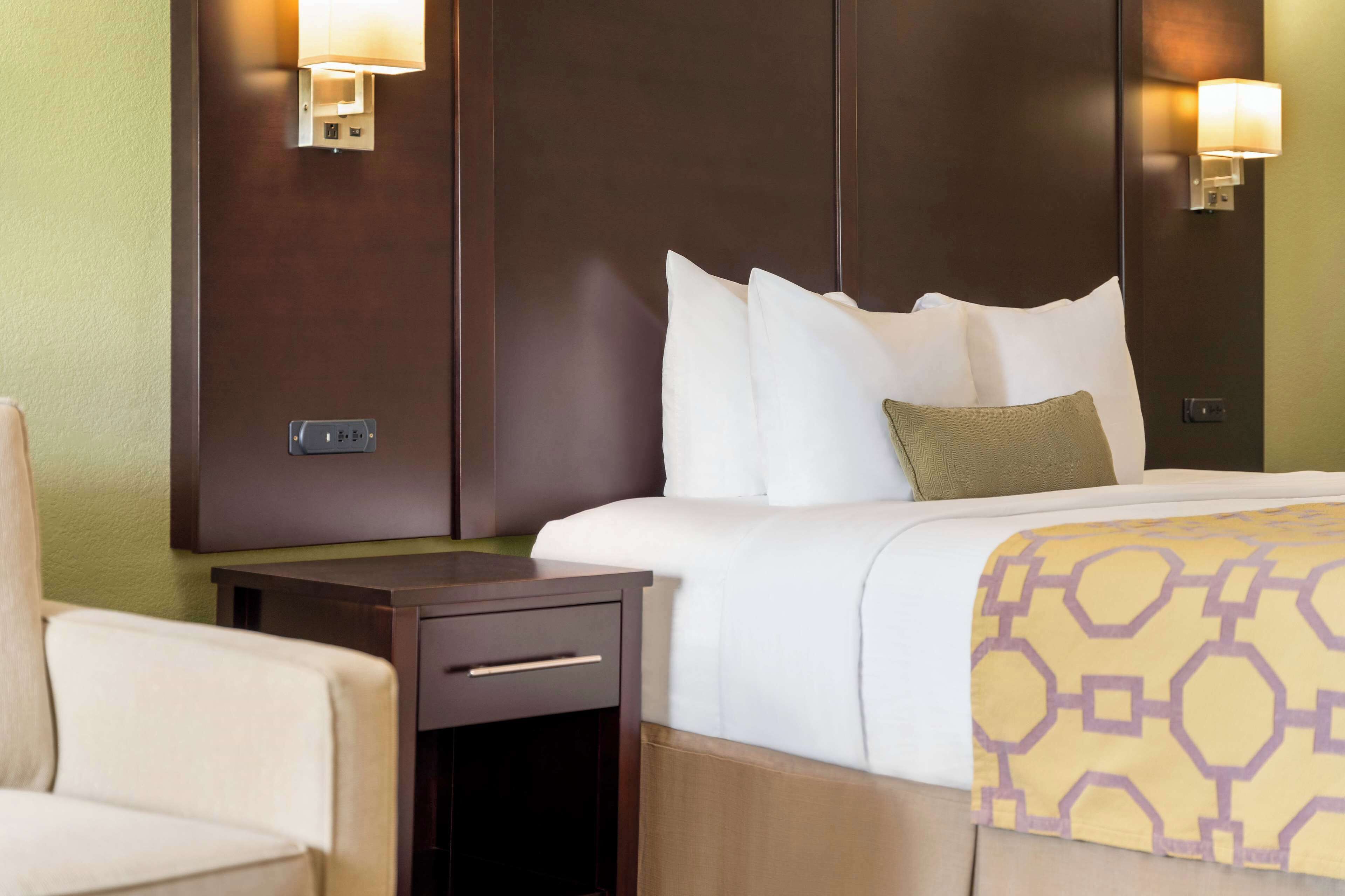 Een hotelkamer met een bed, nachtkastje, lamp en een stoel.