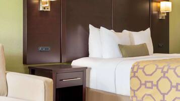 Quarto de hotel com cama, mesa de cabeceira, abajur e uma cadeira.