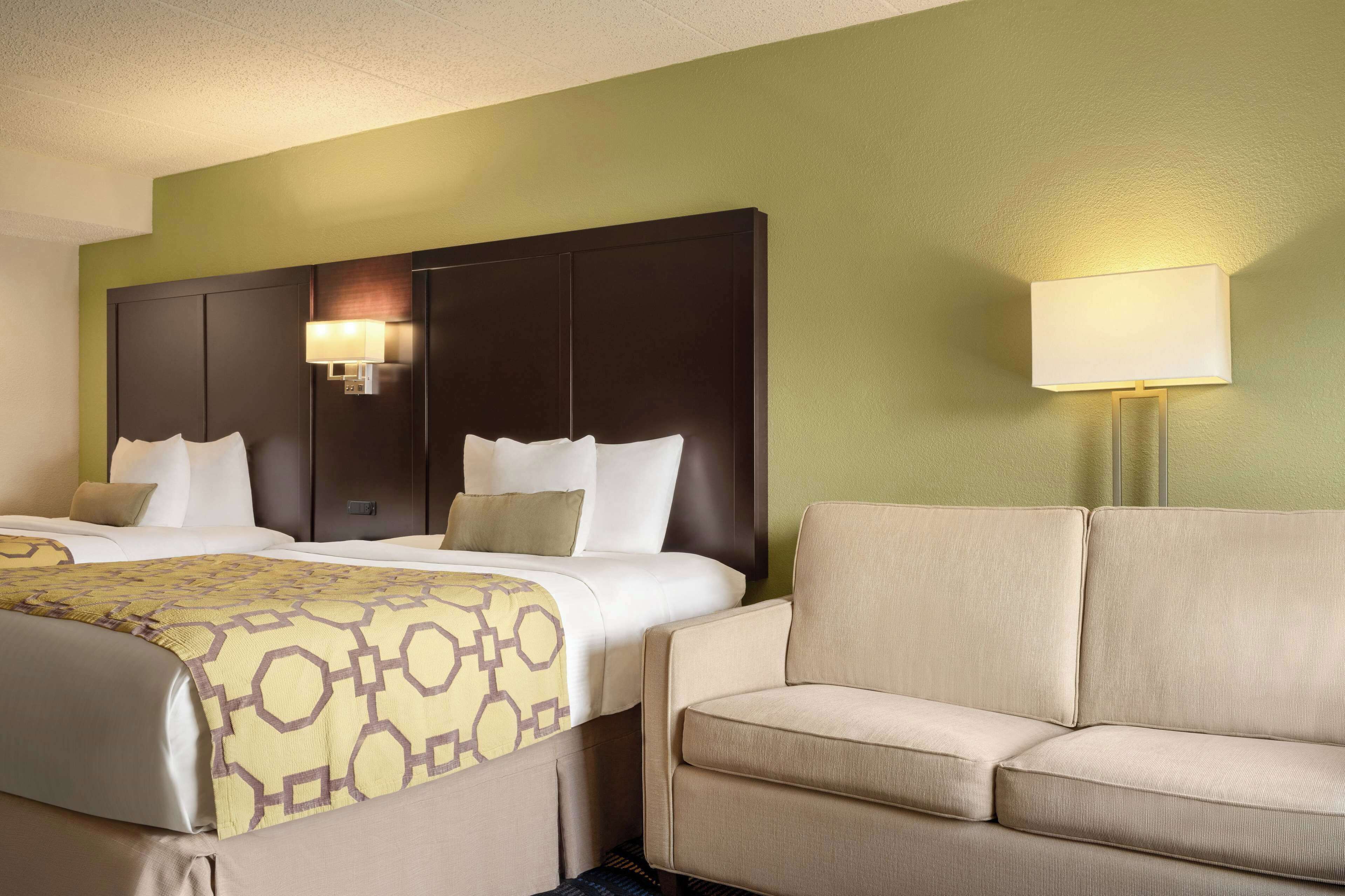 Une chambre d’hôtel avec deux lits, un canapé et une lampe fixée au mur.