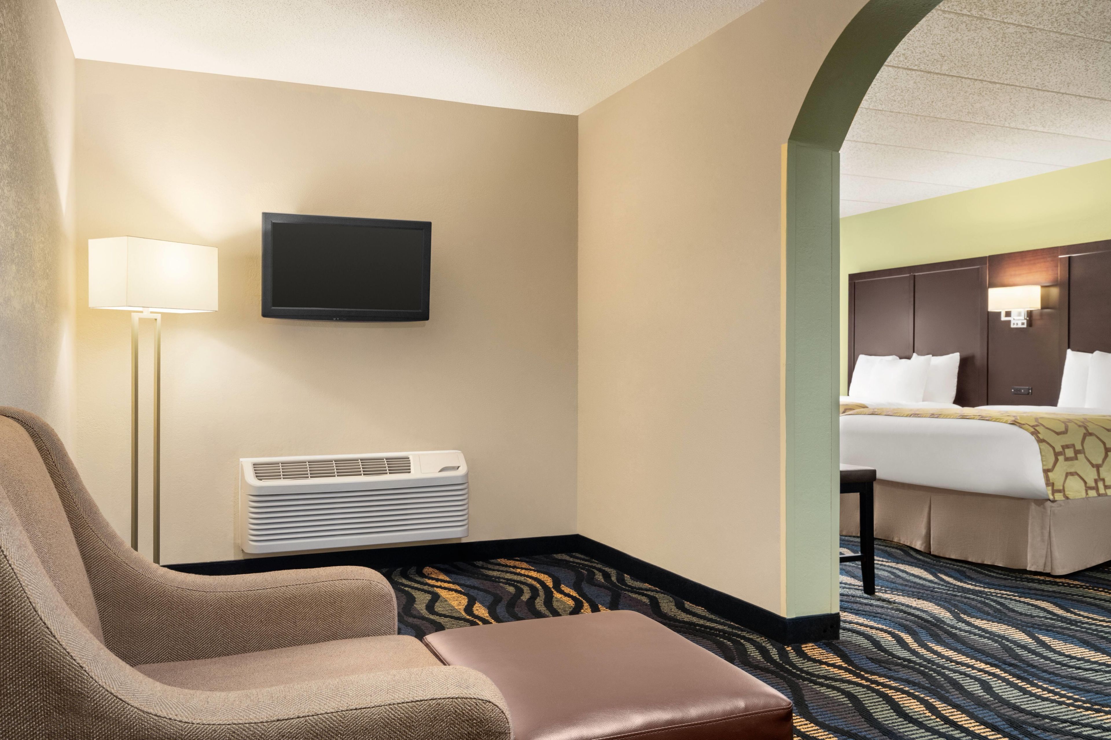 A hotel room with a flat-screen TV, a standing heater, a sofa, and a bed with a patterned bedspread.