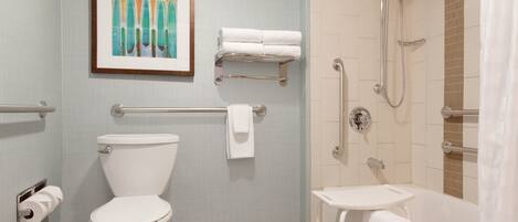 Une salle de bain avec des toilettes, un lavabo et une douche. Un tableau encadré est accroché au mur, et il y a un porte-serviettes avec des serviettes.