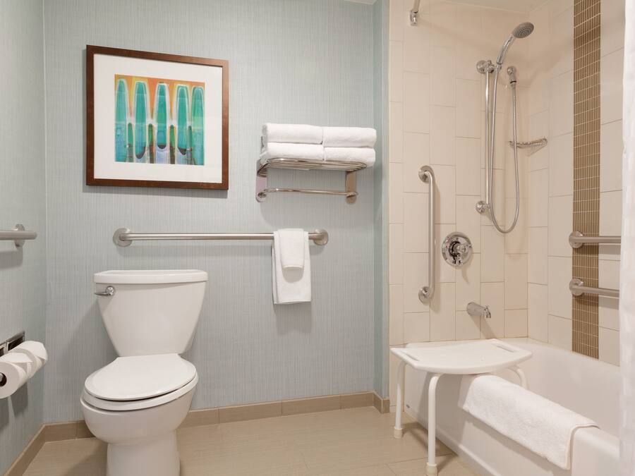 Un baño con inodoro, lavamanos y ducha. Se aprecia un cuadro en la pared y un perchero con toallas.