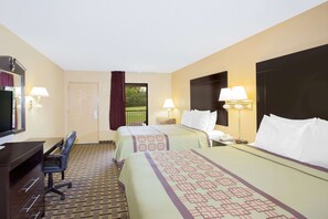 A hotel room with two beds, a desk with a chair, a television, and a window with a view of greenery. - Days Inn by Wyndham Andalusia (Andalusia)